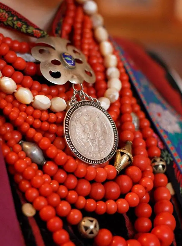 A macro shot of a silver dukach medallion resting on strands of red coral beads