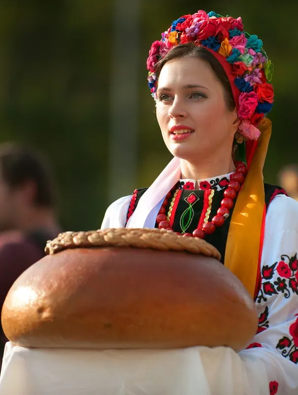 A woman in a floral wreath headdress holding a large ceremonial korovai bread