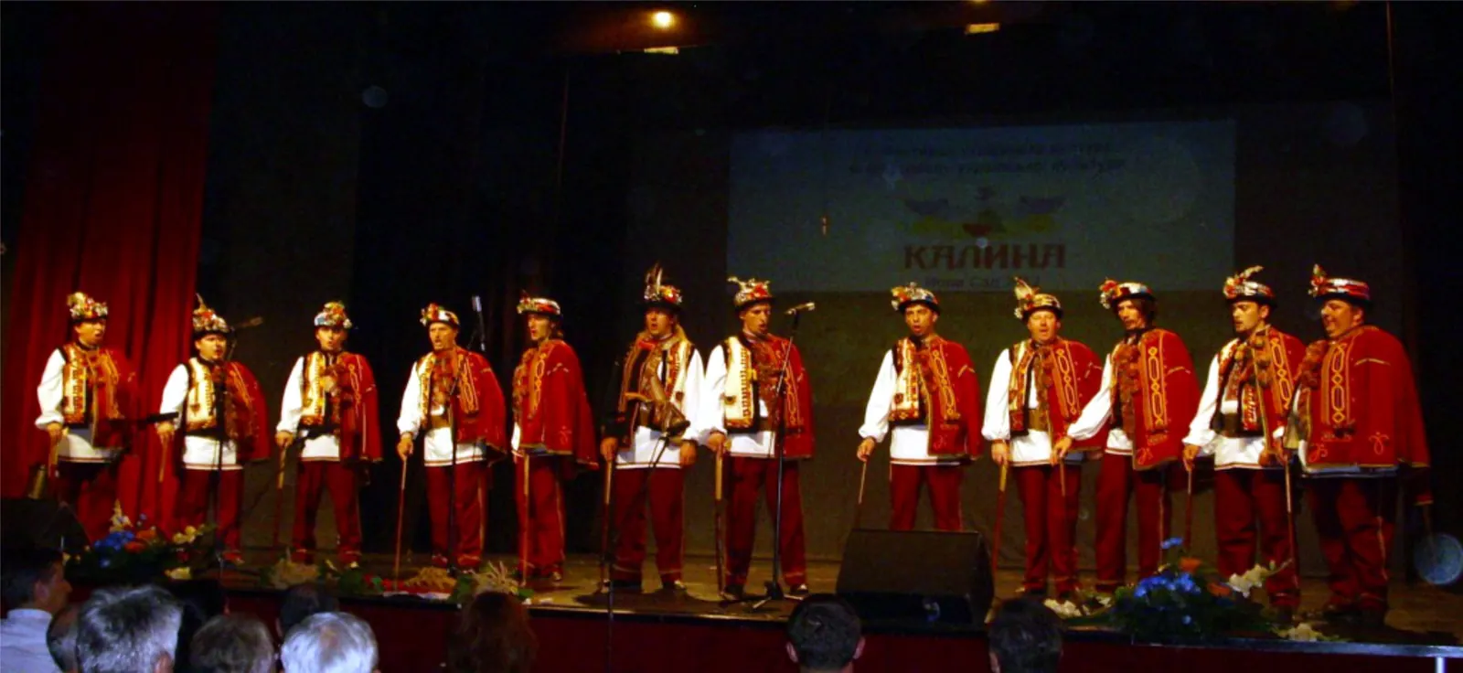 Male singers of a Hutsul ensemble performing on stage in red embroidered vests and feathered hats