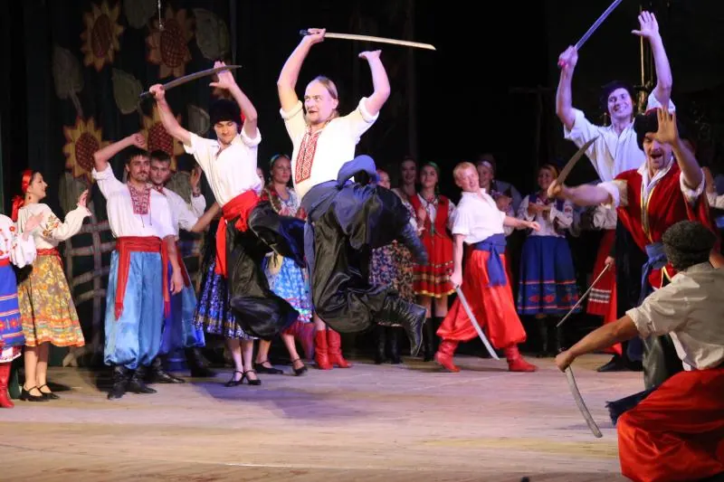 Dancers leaping with raised sabres mid-performance on stage
